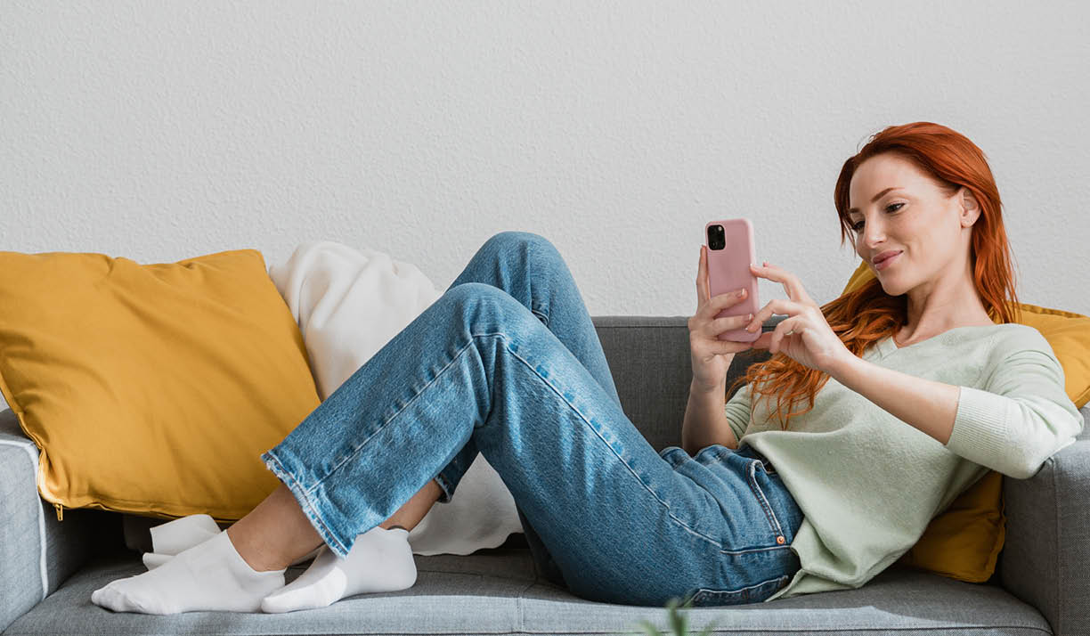 Young woman using smartphone while relaxing on couch at home